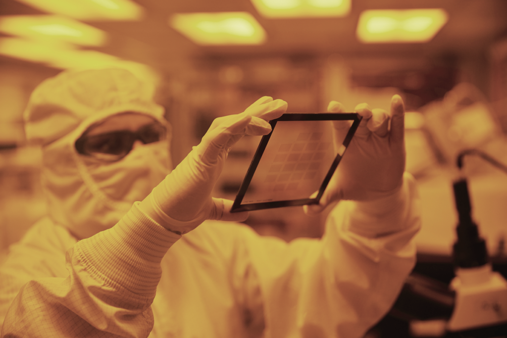 Person in cleanroom suit, with goggles, holding a translucent rectangular object